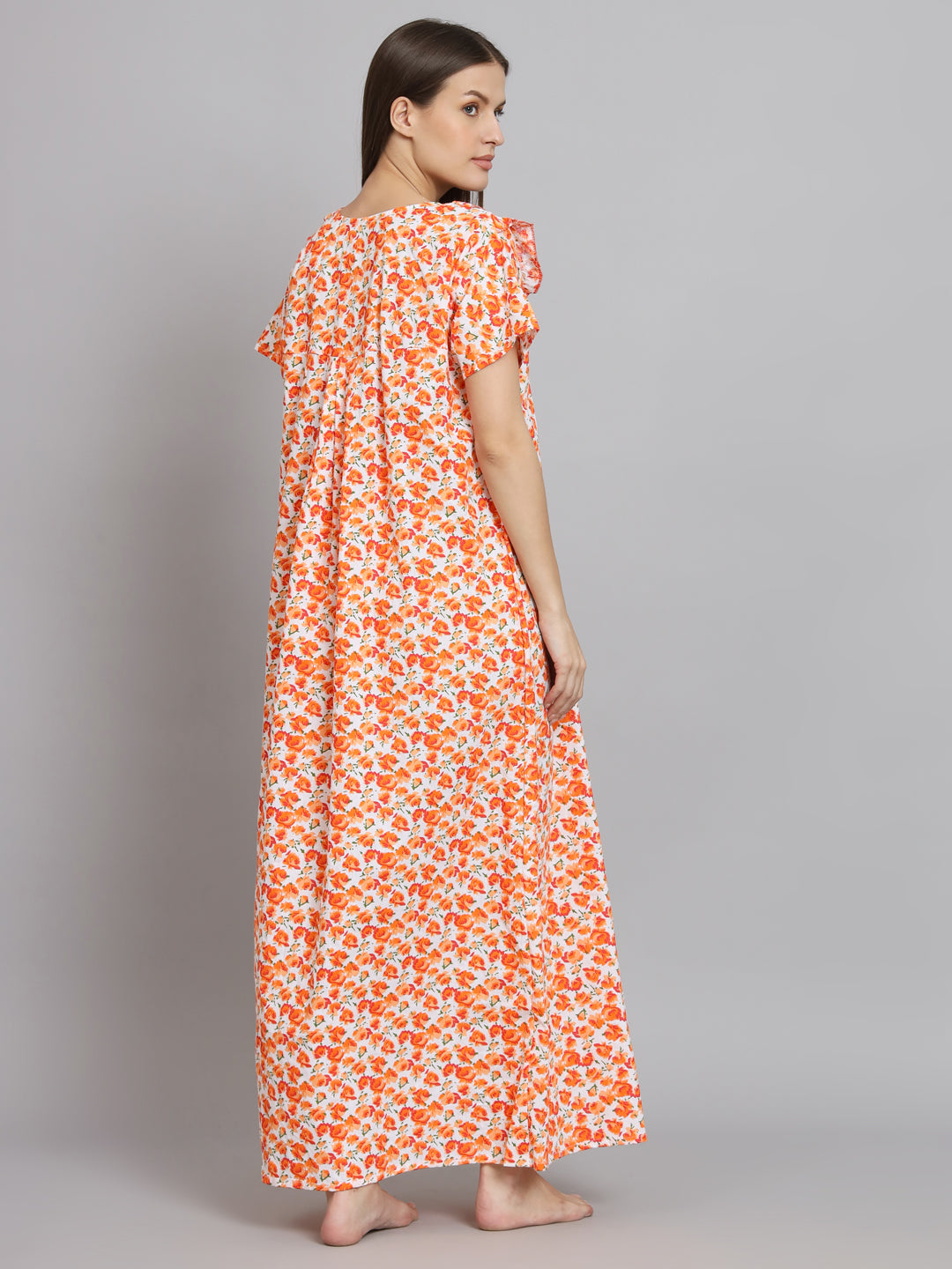 A woman modeling a long, off-the-shoulder maxi dress with a vibrant orange and white floral print, shown from a three-quarters back view against a solid gray studio background.