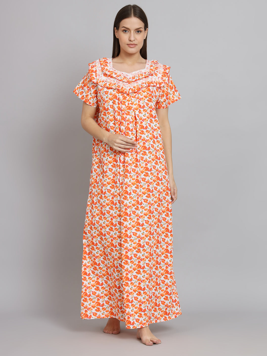 A woman modeling a long-sleeved maxi nightgown with an orange and white floral pattern, standing against a solid gray studio background.