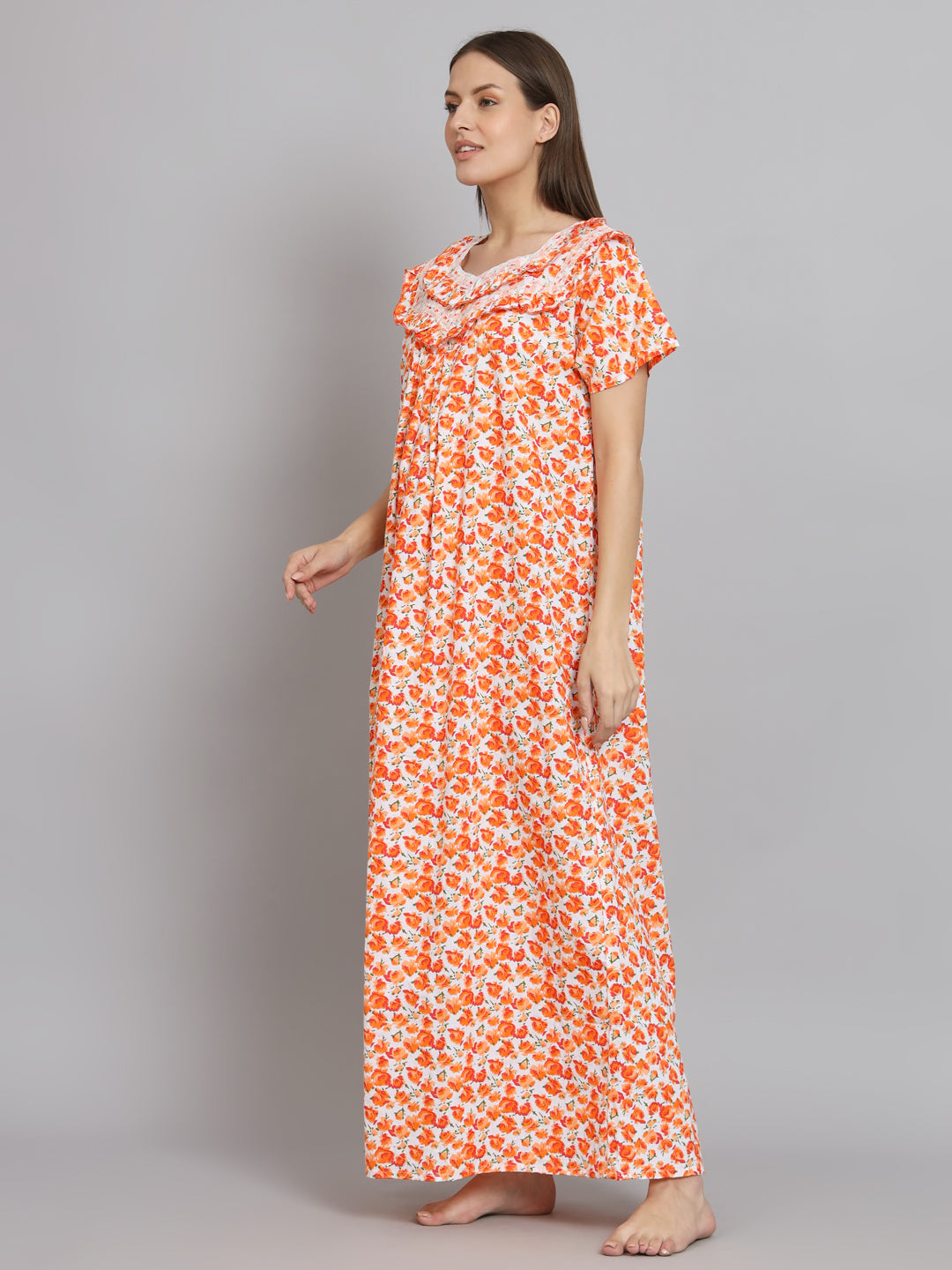 A woman modeling a long, short-sleeved nightgown with an orange and white floral pattern, standing against a solid gray studio background.