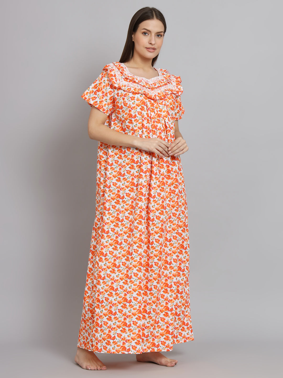 A woman modeling a long, short-sleeved nightgown with an orange and white floral pattern against a solid gray studio background.