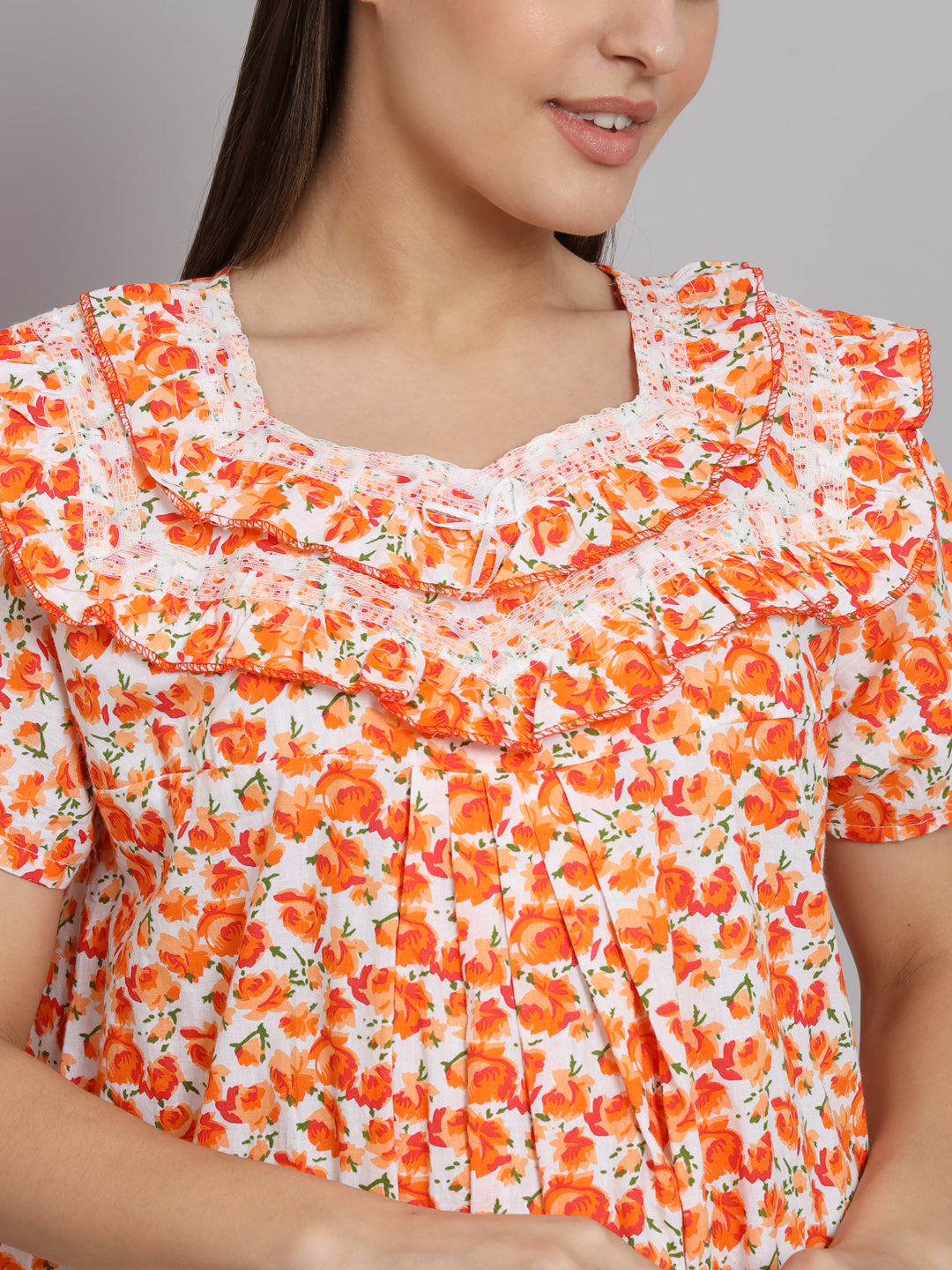 A close-up of a woman wearing a short-sleeve blouse with a white base and an orange floral print, featuring a ruffled scoop neckline.