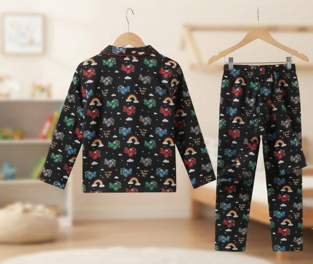 A two-piece children's pajama set hanging on wooden hangers, featuring a long-sleeve top and matching pants in black with a colorful pattern of hearts, rainbows, clouds, and stars. The background is a softly blurred, warm-toned children's bedroom.