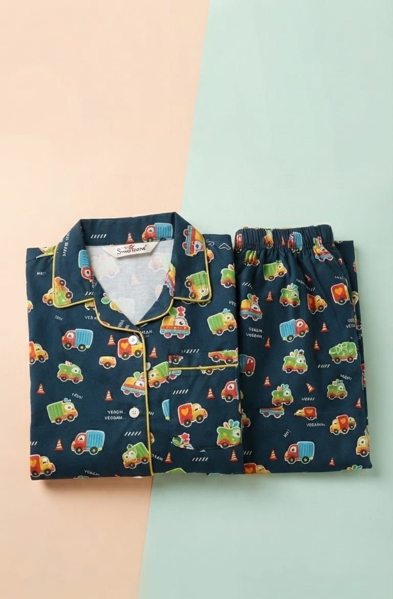 A two-piece children's pajama set featuring a navy blue background with a colorful cartoon truck pattern, laid flat on a split pastel peach and mint green background.