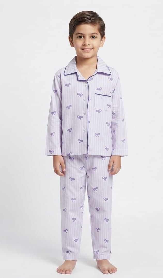 A young boy wearing a two-piece pajama set with a light lavender and white vertical stripe pattern and a purple bow print, standing against a plain white studio background.