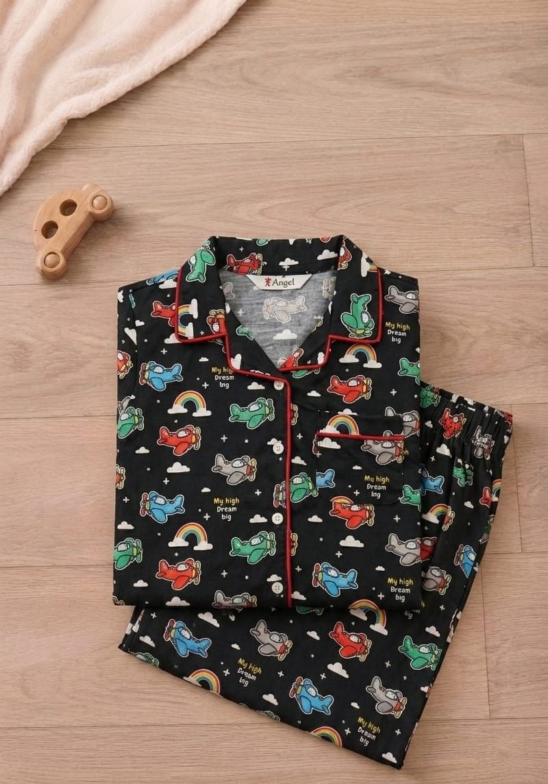 A folded children's pajama set with a black background and a colorful cartoon print of cars, rainbows, and clouds, styled on a light wood floor next to a wooden toy car.