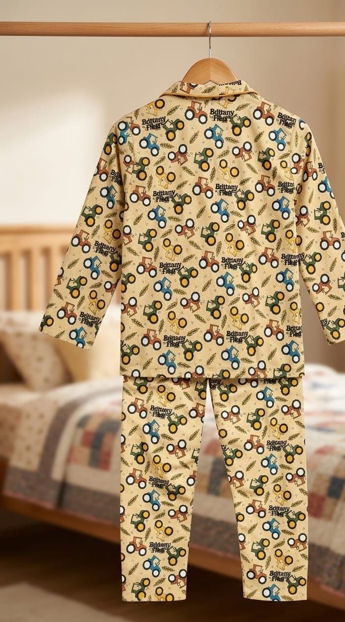 A two-piece children's pajama set hanging on a wooden hanger, featuring a beige background with a colorful tractor pattern. The set includes a long-sleeve top and matching pants, displayed against a softly blurred bedroom background.