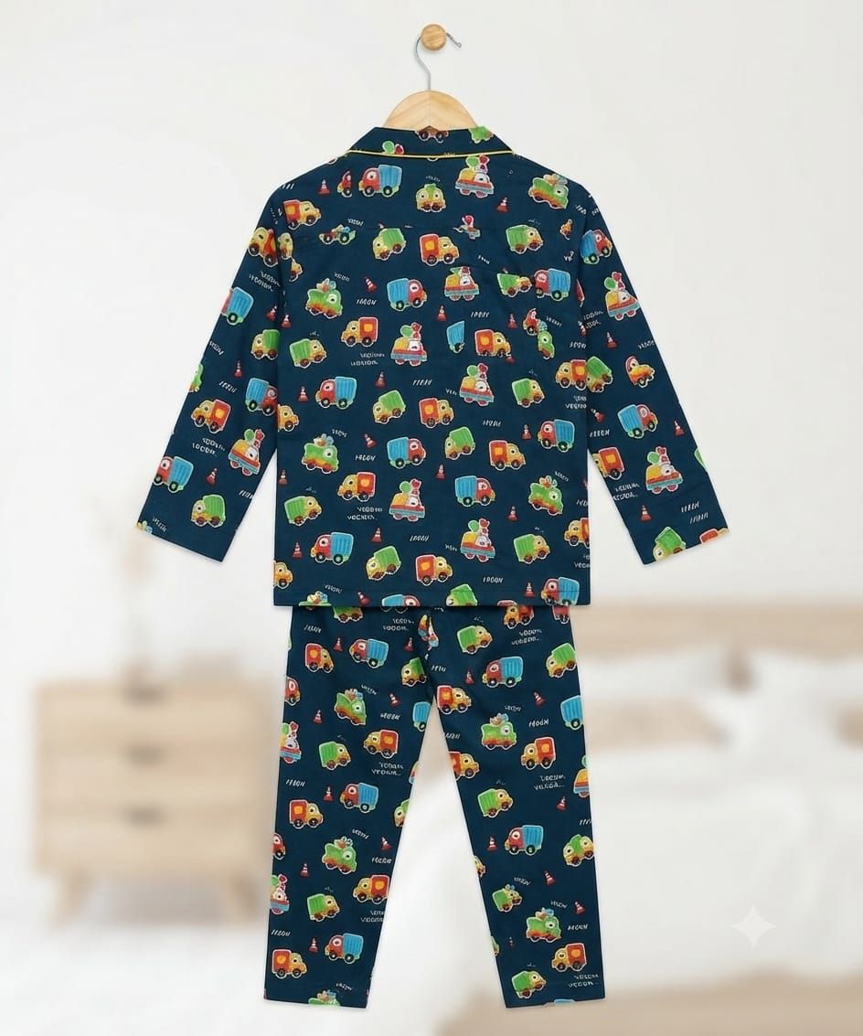 A two-piece children's pajama set hanging on a wooden hanger against a softly blurred bedroom background. The set includes a long-sleeve top and matching pants in dark navy blue with an allover colorful cartoon train pattern.