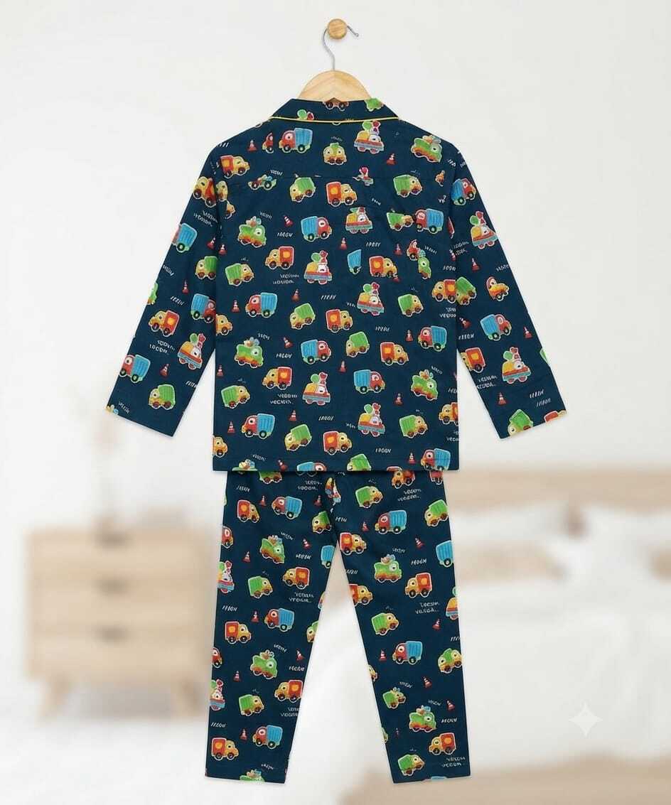 A two-piece children's pajama set hanging on a wooden hanger against a softly blurred bedroom background. The set includes a long-sleeve top and matching pants in dark navy blue with an all-over repeating print of colorful toy cars and small illustrated figures.