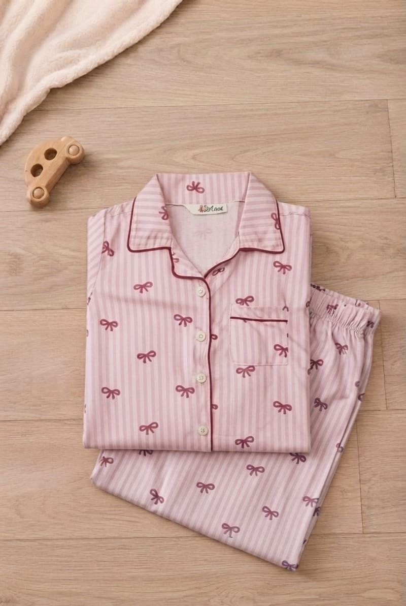A folded pink pajama set with vertical stripes and small bow prints, displayed on a light wood floor next to a small wooden toy car and a soft cream blanket.