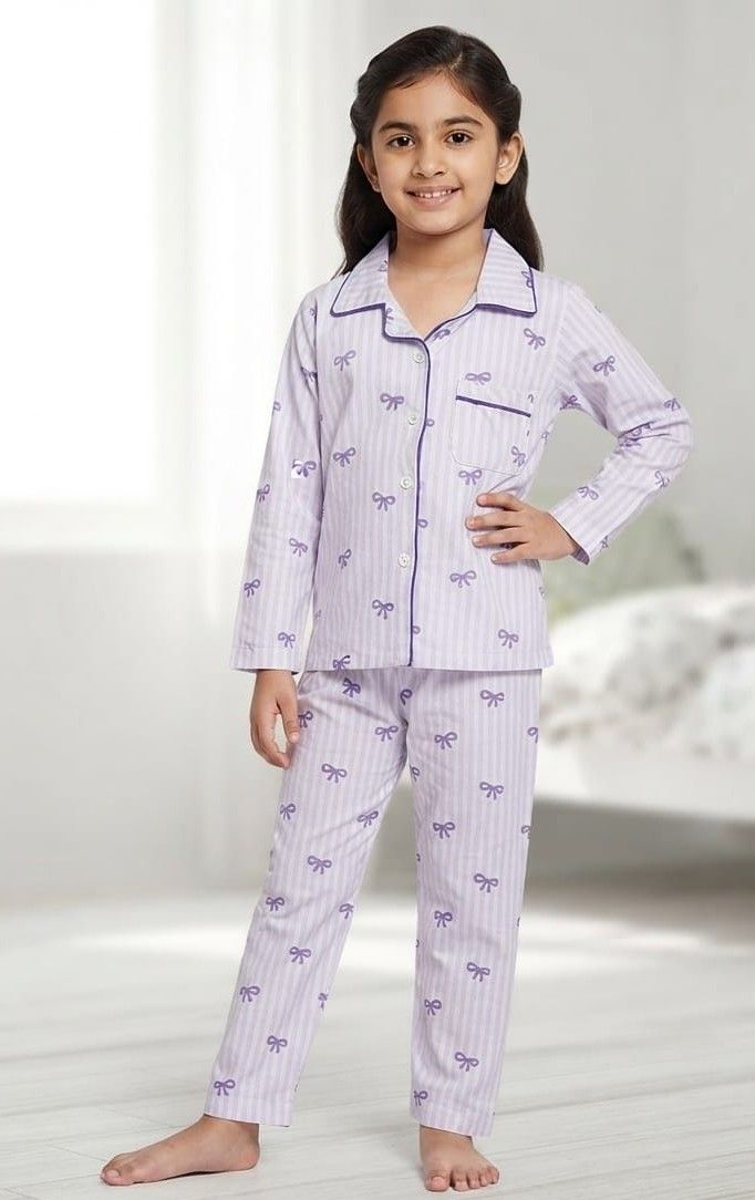 A young girl modeling a two-piece pajama set with light lavender and white vertical stripes, decorated with small purple bow prints and purple piping details.