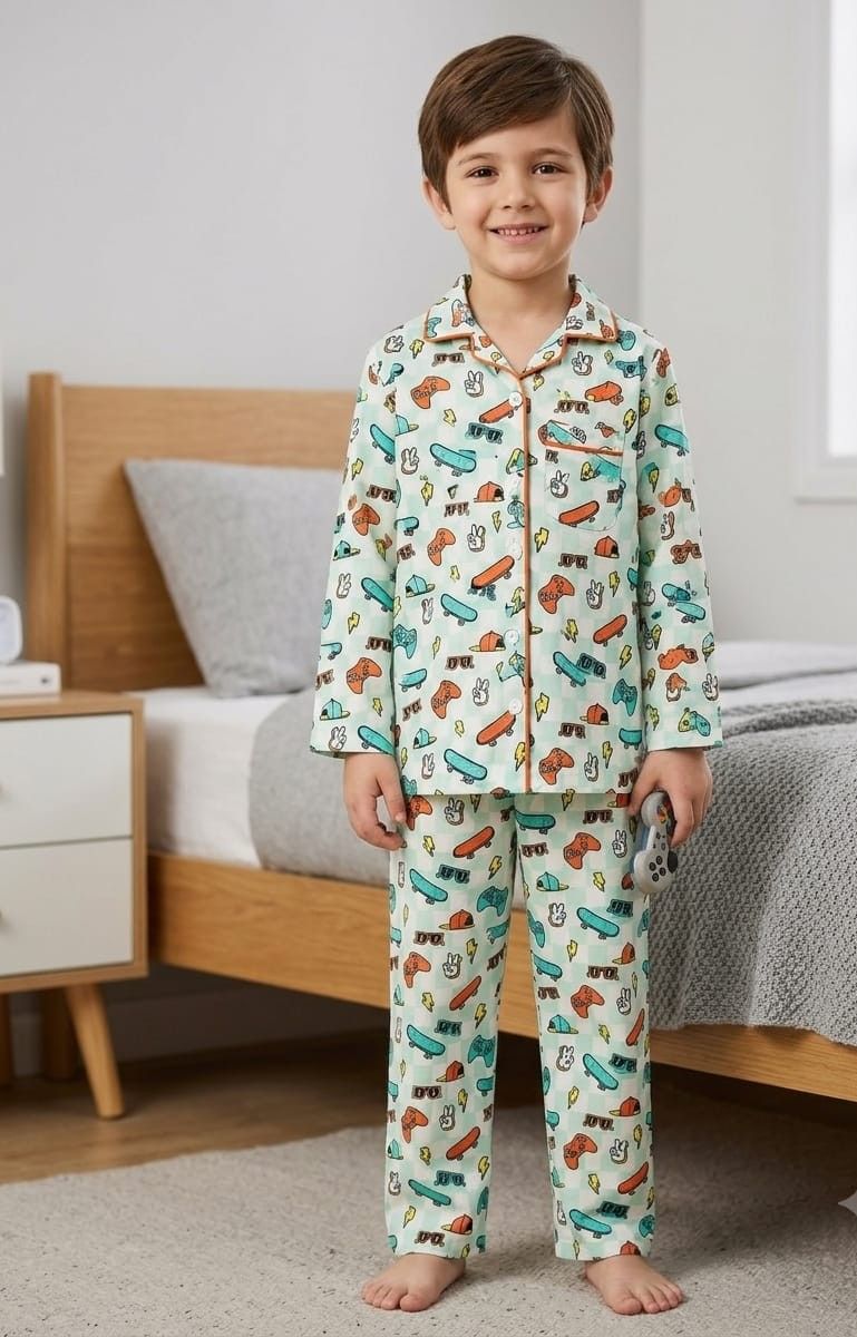 A young boy stands in a bedroom wearing a two-piece pajama set with a light green background and a colorful cartoon car pattern. The set includes a long-sleeve button-up shirt and matching pants.