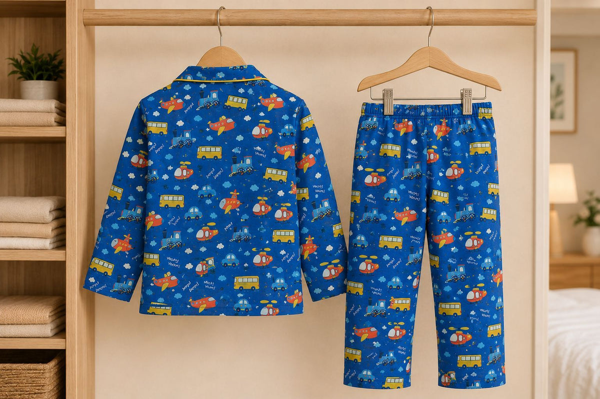 A two-piece children's pajama set with a blue background and a colorful pattern of toy vehicles, hanging on wooden hangers inside a wooden closet. The set includes a long-sleeve top and matching pants.