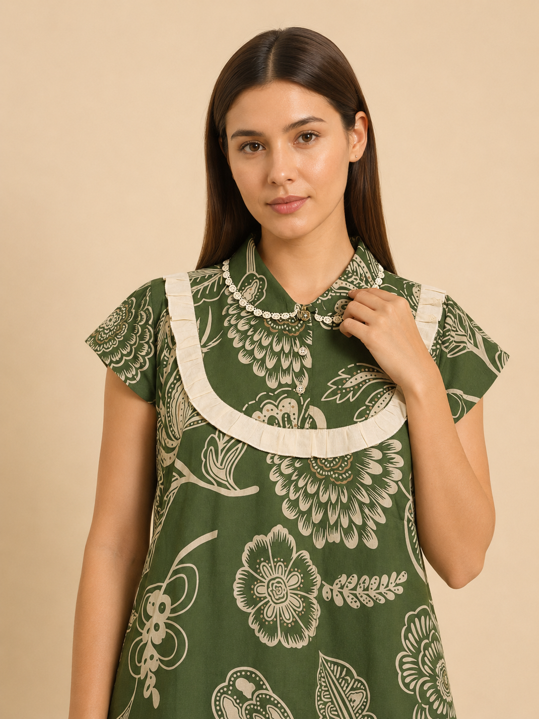 A woman wearing a green short-sleeve dress with a cream floral block print and a wide cream ruffled collar, posed against a solid beige background.