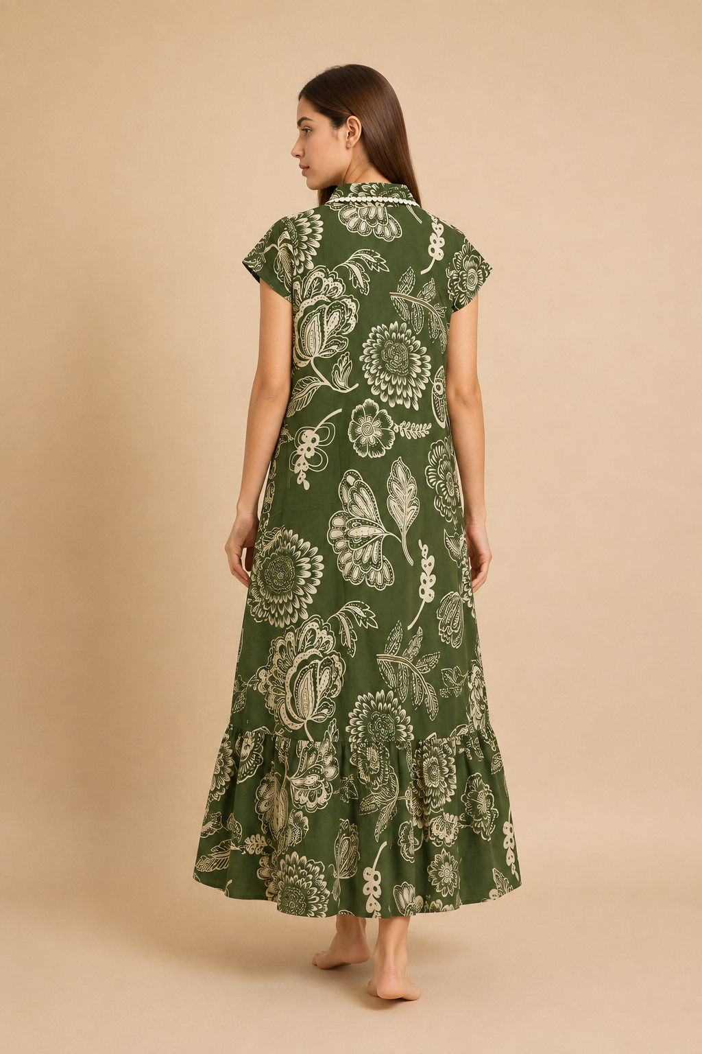 A woman viewed from the back wearing a green midi dress with a cream floral print, standing against a solid beige studio background.