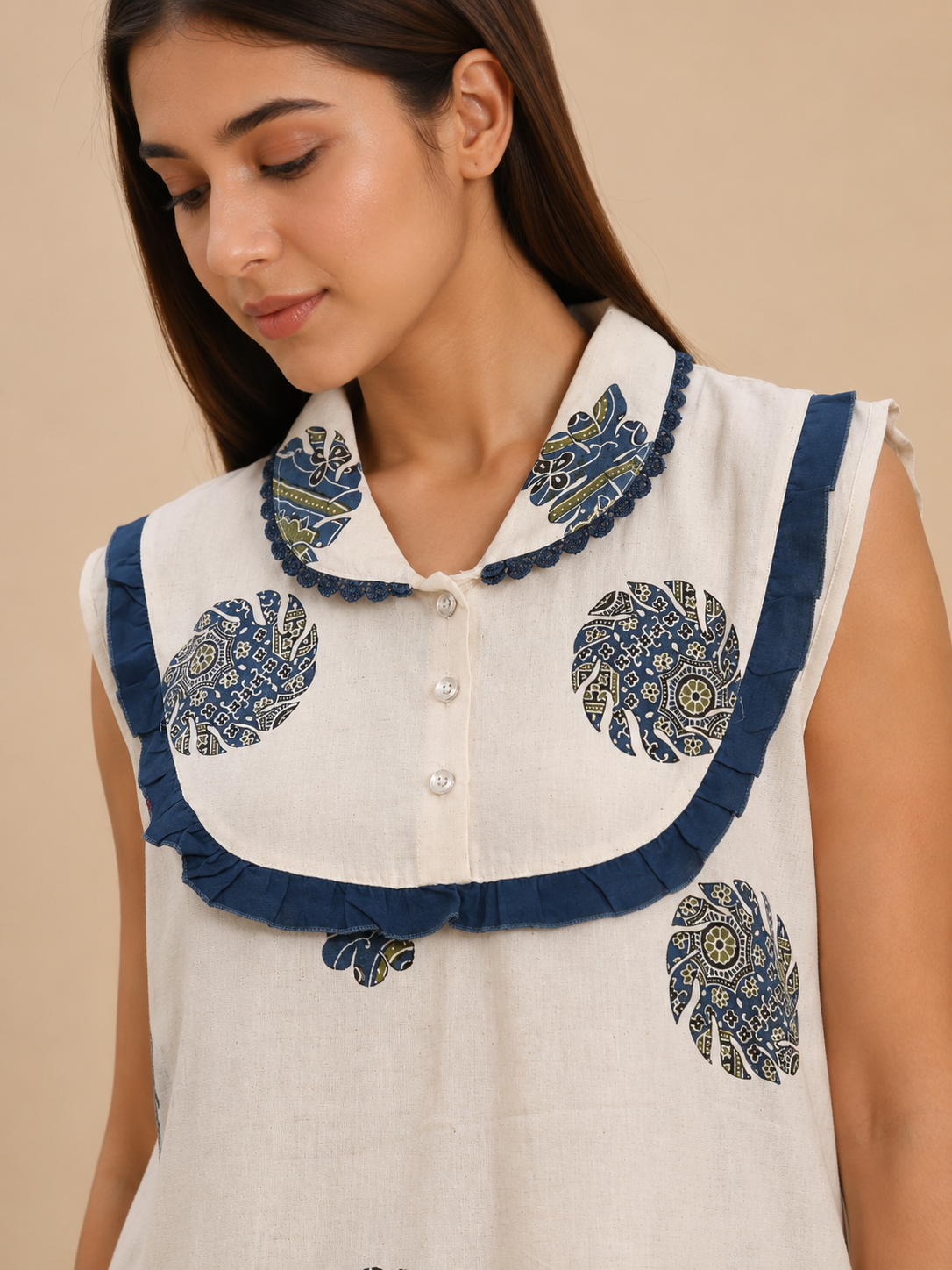 A close-up of a woman wearing a sleeveless white top with a large ruffled collar in navy blue and beige, featuring circular botanical prints.