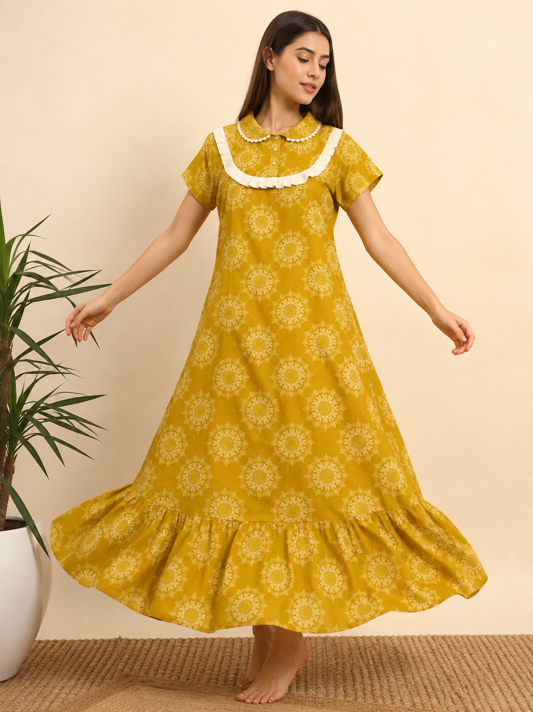 A woman modeling a yellow midi-length dress with a white floral mandala pattern, a white ruffled Peter Pan collar, and short sleeves, standing barefoot on a woven rug against a beige wall.