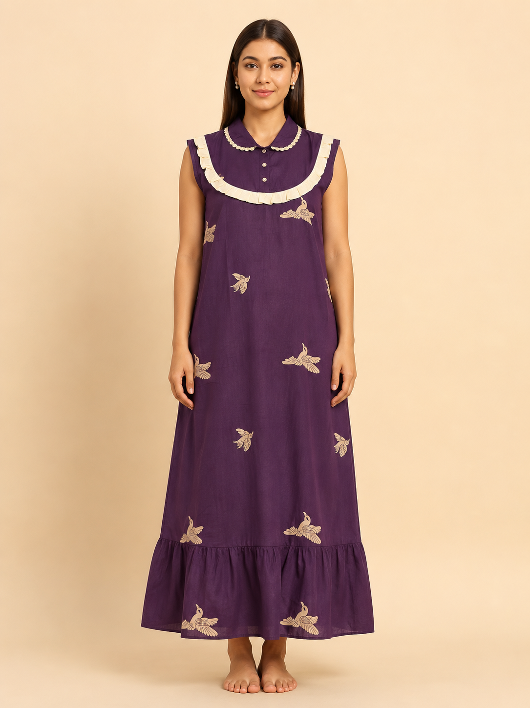 A woman modeling a sleeveless purple maxi dress with a white ruffled collar and beige bird embroidery, standing against a solid beige background.