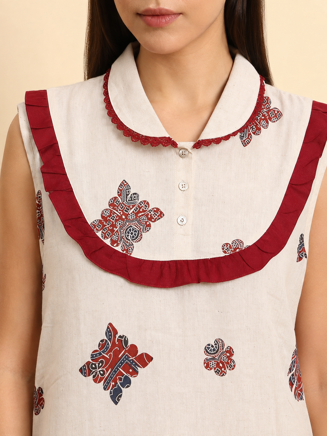 A close-up of a sleeveless white kurta featuring red ruffled trim around the collar and button placket, with red and navy blue floral block prints.