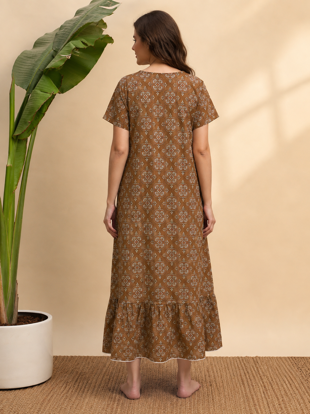 A woman stands barefoot indoors wearing a brown short-sleeve maxi dress.