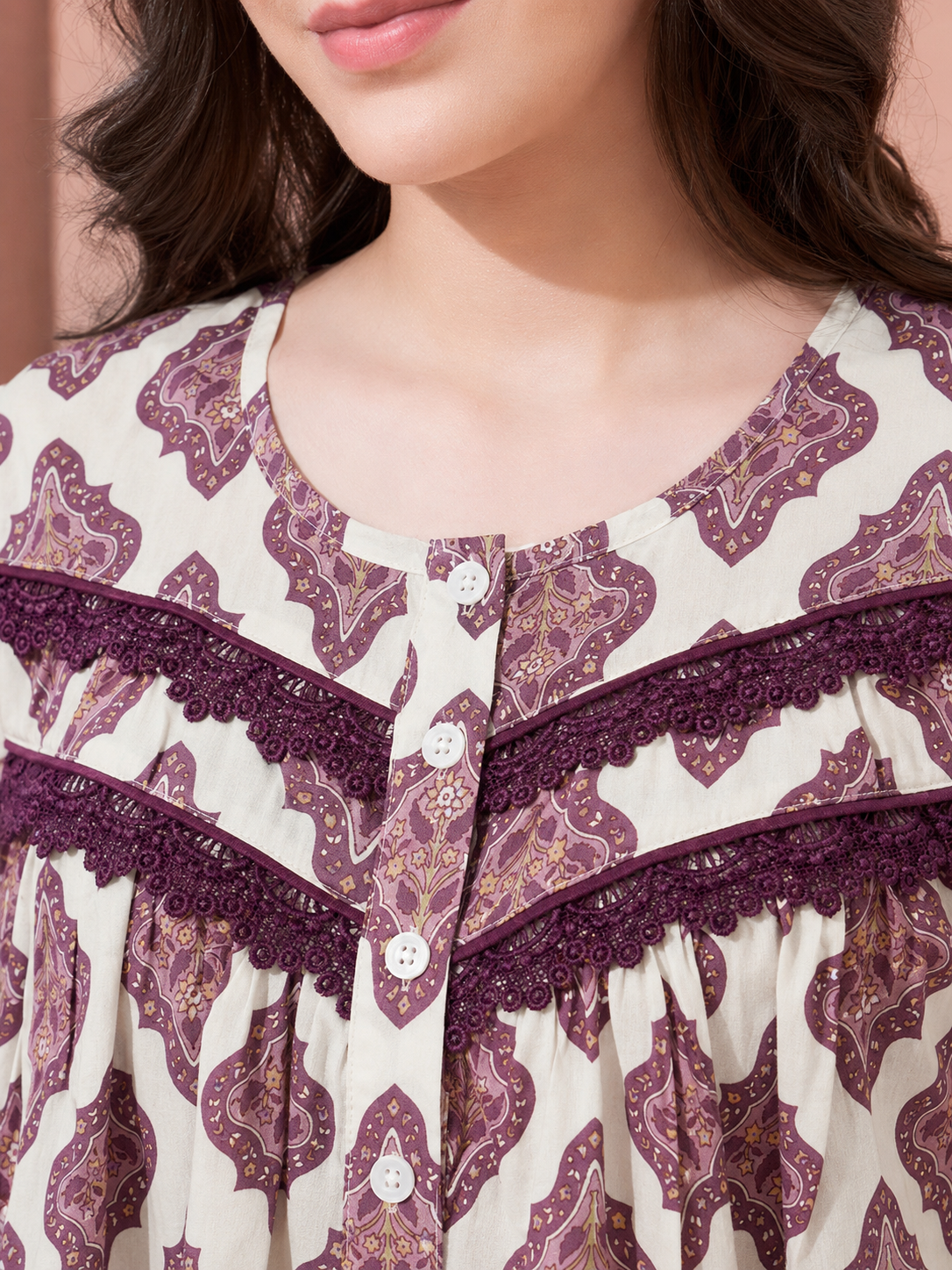 Close-up of a woman wearing a cream-colored blouse with a purple paisley pattern and matching purple lace trim along the neckline and front buttons.