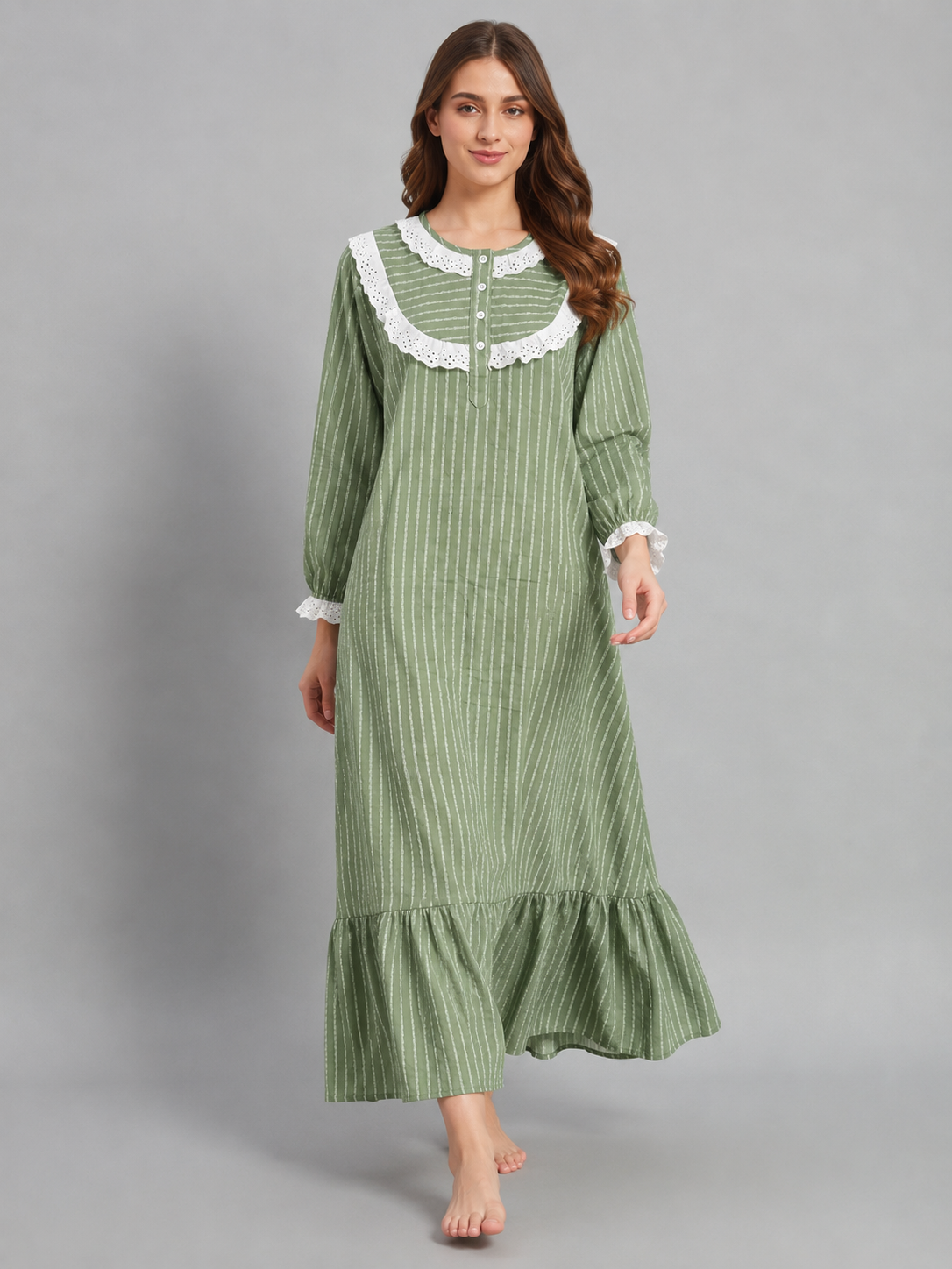 A woman modeling a green and white vertically striped long-sleeve nightgown with a white lace collar and cuffs, standing against a solid gray studio background.