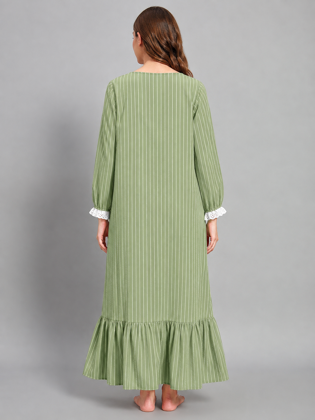 A woman viewed from the back wearing a sage green maxi dress with thin vertical stripes, white lace cuff trim, and a ruffled hem, set against a solid gray studio background.