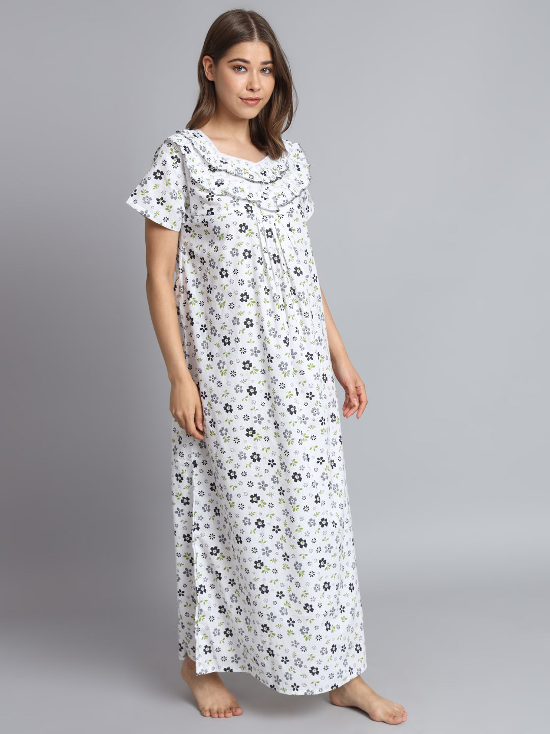 A woman modeling a long white nightgown with a small black and gray floral print, standing against a solid gray studio background.